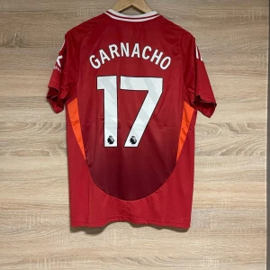 Manchester United med Garnacho 17 L - Säljer en röd fotbollströja från Adidas med Garnacho och nummer 17 på ryggen. Tröjan har korta ärmar och Manchester Uniteds emblem på bröstet. Den har vita detaljer och sponsorn Snapdragon tryckt på framsidan.