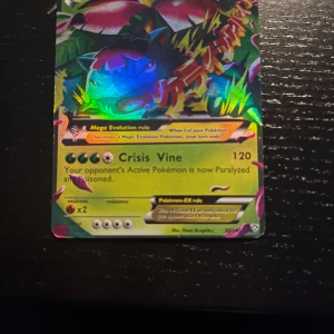 Mega Venusaur EX Pokémonkort - Säljer ett Mega Venusaur EX Pokémonkort med färgglad och glansig design. Kortet har en kraftfull attack som heter 'Crisis Vine' och kan paralysera och förgifta motståndarens Pokémon. Perfekt för samlare eller spelare som vill förstärka sin kortlek.