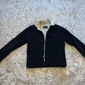 Svart manchesterjacka med teddyfoder - Säljer en snygg svart manchesterjacka från Abercrombie & Fitch. Jackan har ett mysigt teddyfoder och knappar framtill. Perfekt för kyligare dagar med sin stilrena design och praktiska bröstfickor.