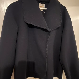 Marinblå kappa från Gina Tricot - Snygg marinblå kappa från Gina Tricot med en stilren design. Kappan har en bred krage och är perfekt för en chic look. Den är långärmad och har en elegant passform som passar till många tillfällen.