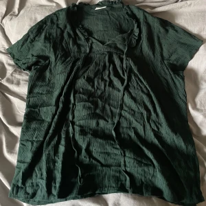 Mörkgrön blus med volangdetaljer - Säljer en mörkgrön blus med volangdetaljer vid halsringningen. Använd fåtal gånger.