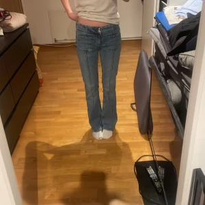 Blå jeans från Gina Tricot - Snygga blå jeans från Gina Tricot i storlek 158. Dom är låg midjadeoch  ut svängda. Jeansen har en dragkedja och knappar framtill för enkel stängning. Perfekta för en avslappnad stil.