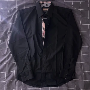 Svart skjorta från Burberry - Snygg svart skjorta från Burberry med klassisk krage och knappar framtill. Skjortan har långa ärmar och en stilren design. Perfekt för en elegant look.