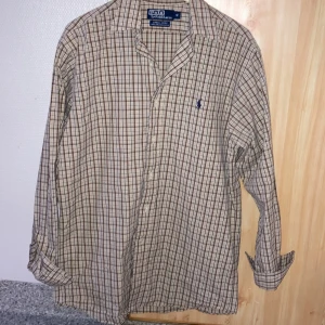 Snygg rutig raffe skjorta. Tar även emot byten. -  Snygg rutig skjorta från Polo Ralph Lauren i beige, brun och blå. Perfekt för en stilren look. Den är i storlek S men den sitter som en M. Jag tar även emot byten om någon är intresserad så var inte rädda för att ställa frågor utan tvek. Priset är ej hugget i sten
