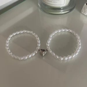 Pärlarmband med hjärtdetalj - Säljer ett par superfina pärlarmband med en söt hjärtdetalj i mitten. Armbanden är elastiska. De vita pärlorna ger en klassisk och elegant look. Perfekt som present eller för att piffa upp din egen smyckessa