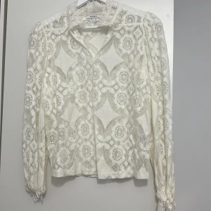 Vit spetsblus från Rosebud - Säljer en superfin vit spetsblus från Rosebud i storlek S. Blusen har ett vackert blommigt mönster och långa ärmar med spetsdetaljer vid ärmsluten. Perfekt för en elegant look till både vardag och fest!