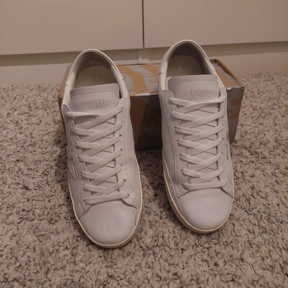 Säljer ett par stilrena vita skor från Golden goose. Skick är 9,5/10 defekt kan man se på bild 4. Har även box och orderbekräftelse från minto. Nypris ligger på 5500 , jag säljer för endast 2600. Om ni har några frågor är det bara att skriva.. Skor.