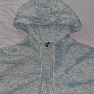 Grå croppad hoodie - Säljer denna superfina grå croppade hoodie med ett subtilt batik mönster i ljusblått. Den har en justerbar huva med dragsko och långa ärmar med ribbade muddar. Säljer den då jag måste rensa min garderob.