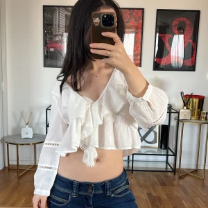 Vit blus med volanger Zara  - Säljer en superfin vit blus från Zara med volanger och v-ringning. Den är croppad och har långa ärmar med spetsdetaljer. Perfekt för en somrig look eller en festkväll!💓 Använd endast enstaka gång.