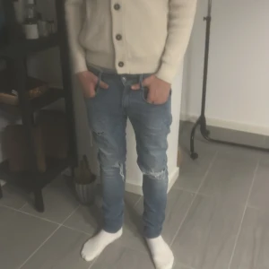 Replay jeans - Säljer ett par snygga blå replay jeans med slitningar på knäna. De har en klassisk femficksdesign och en bekväm passform. Perfekta för en avslappnad stil! 