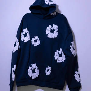 Denim Tears Hoodie - Helt ny Denim Tears Hoodie med vita mönster över hela plagget. Hoodien har långa ärmar och en bekväm huva. Perfekt för en avslappnad stil.