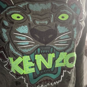 Svart tröja med tigerbroderi från Kenzo - Snygg svart tröja från Kenzo med ett stort, färgglatt tigerbroderi på framsidan. Tröjan har en cool design med gröna och blå detaljer som verkligen sticker ut. Perfekt för dig som vill ha något unikt i garderoben!