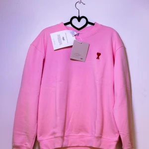 Ami Paris Sweatshirt - Helt ny Ami Sweatshirt med ett rött hjärta broderat på bröstet. Tröjan har en klassisk rund halsringning. Perfekt för en avslappnad stil. 😊