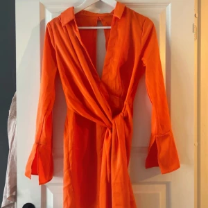 Orange omlottklänning - Snygg orange omlottklänning med långa ärmar och knytning i midjan. Perfekt för en färgstark look.
