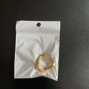 Guldiga örhängen i unik form - Snygga guldiga örhängen med en modern och unik form. Perfekta för att ge en stilren touch till din outfit. De har en slät och glänsande yta som fångar ljuset vackert.