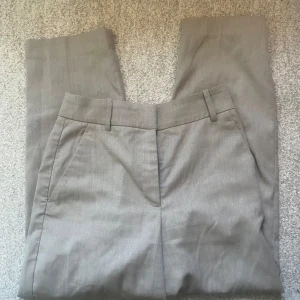 Grå kostymbyxor från H&M 36 - Snygga grå kostymbyxor från H&M med en klassisk design. Byxorna har hällor för bälte och två bakfickor med passpoal. Perfekta för en stilren look. Storlek 36 med en croppad modell