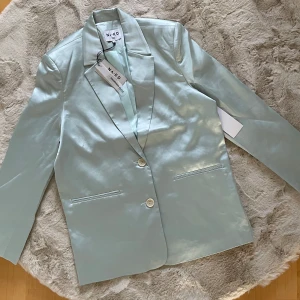 Ljusblå kavaj från NA-KD 36 oversize oanvänd  - Snygg ljusblå kavaj från NA-KD med en stilren design. Kavajen har två knappar framtill och klassiska slag. Perfekt för att ge en elegant touch till din outfit.