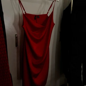 Röd axelbandslös klänning - Snygg röd klänning med smala axelband och draperad design. Perfekt för en kväll ute eller en speciell tillställning. Klänningen har en figurnära passform som framhäver silhuetten.