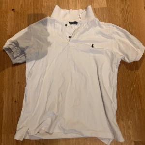 Vit Polo RL pikétröja - Snygg vit pikétröja med klassisk krage och knappar framtill. Tröjan har en liten broderad RL loggo på bröstet och korta ärmar. Perfekt för en avslappnad stil. Storlek L men passar perfekt till M.