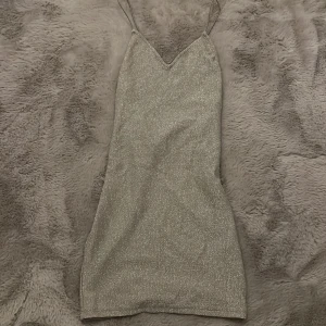 Glittrig klänning från H&M - Snygg glittrig klänning från H&M i silver med smala axelband och v-ringad design. Perfekt för en festlig kväll. Materialet är en blandning av polyamid och elastan för en bekväm passform.