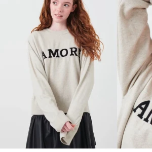 Beige tröja med texten AMORE - Säljer en beige tröja med svart text 'AMORE' på framsidan. Tröjan har en avslappnad passform med långa ärmar och ribbade muddar. Perfekt för en mysig och stilren look. Orginal pris 229kr