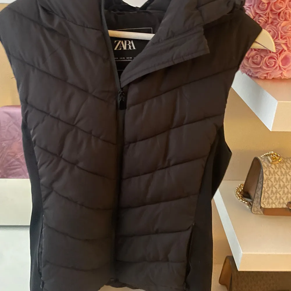 Snygg svart dunväst från Zara med dragkedja och huva. Perfekt för kyliga dagar och enkel att matcha med olika outfits.. Takit.