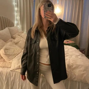 Svart skinnjacka - Snygg svart skinnjacka med knappar och klassisk krage. Perfekt för en stilren look. 