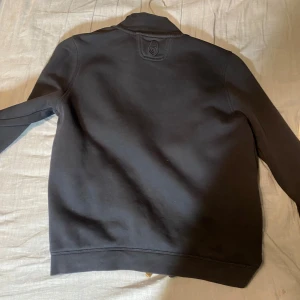Blå tröja från Sail Racing - Snygg svart tröja från Sail Racing med dragkedja framtill. Tröjan har en stilren design med hög krage och långa ärmar. Perfekt för en sportig look.