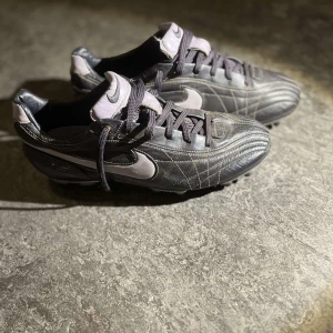 Svarta fotbollsskor från Nike - Snygga svarta fotbollsskor från Nike med vita detaljer och snörning. Skorna har en robust sula med dobbar för bra grepp på planen. Perfekta för fotbollsträning och matcher.