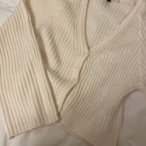 Beige ribbad kofta från HM - Säljer en stilren beige kofta från HM. Den är ribbad med en v-ringad design och knappar framtill. Perfekt för lager-på-lager under kyligare dagar. Passar till både jeans och kjol!