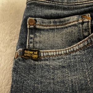 Blå jeans från Tiger of Sweden - Snygga blå jeans från Tiger of Sweden med klassisk femficksdesign och läderdetalj vid midjan. Perfekta för en stilren look. Modellen heter pisterlo. passar bäst till dig mellan 158-170