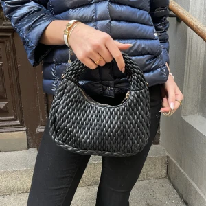 Svart flätad handväska - Snygg svart handväska med mönstrad design och dragkedja. Väskan har även ett långt axelband till! ❤️perfekt till både vardags och fest!