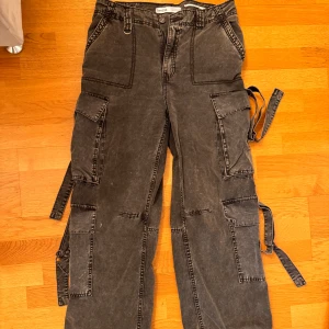 Grå cargobyxor från Bershka - Snygga grå cargobyxor från Bershka med flera praktiska fickor och en cool, avslappnad stil. Byxorna har en dragkedja och knapp framtill. Storlek 40, men skulle säga att de skulle passa en 36,38 för en mer baggy look. 