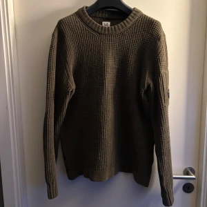 C.P Company stickad tröja - Säljer en olivgrön stickad tröja från C.P. Company. Tröjan har en grovstickad textur och långa ärmar. Perfekt för kyligare dagar med sin stilrena design och bekväma passform.