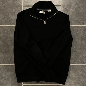 Svart tröja med dragkedja från Jack & Jones - Säljer en stilren svart tröja från Jack & Jones med dragkedja vid halsen. Perfekt för en avslappnad look. Tröjan är i storlek S och passar bra till både vardag och chill.