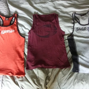 Tre linnen från GASP - Säljer tre linnen från GASP i storlek M. Ett orange med svarta kanter, ett vinrött med ribbad textur och ett grått med svarta detaljer. Perfekta för träning eller en avslappnad dag.