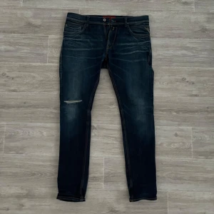 Mörkblå Replay jeans - Snygga mörkblå jeans med en slitning på ena benet. De har en klassisk femficksdesign och en knappgylf. Dem är ifrån Replay