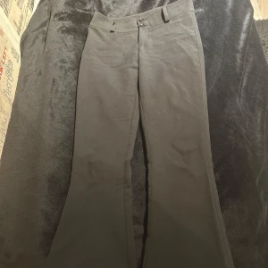 Svarta low y2k bootcut byxor  - Snygga svarta byxor från Gina Tricot med bootcut-stil. Byxorna har en klassisk design med knappar fram och fickor bak. Perfekta för en stilren look.
