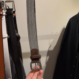Grått flätat bälte onsize - Snyggt grått flätat bälte med bruna skinn-detaljer och silverfärgat spänne. Perfekt för att ge en stilren touch till din outfit.