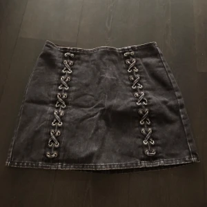 Svart kjol med snörning från H&M - Snygg svart kortkjol från H&M med snörningsdetalj på framsidan och dragkedja där bak som inte längre kommer till användning. 