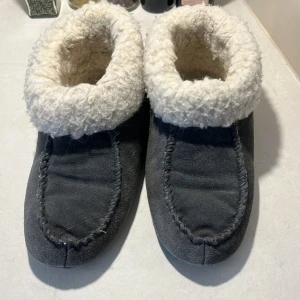 Grå tofflor med vit foder 38-40 - Mysiga grå tofflor med mjukt vitt foder. Perfekta för att hålla fötterna varma under kalla dagar. 
