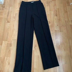 Svarta kostymbyxor från NA-KD - Snygga svarta kostymbyxor från NA-KD med hög midja och stilrena pressveck. Byxorna har en rak passform och slitsar vid bensluten som ger en modern touch. Endast använda vid ett tillfälle!