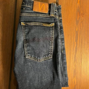 Mörkblå jeans från Nudie Jeans - Snygga mörkblå jeans från Nudie Jeans med klassisk femficksdesign och kontrastsömmar. Perfekta för en stilren look. Passar bra till både vardag och mer uppklädda tillfällen.