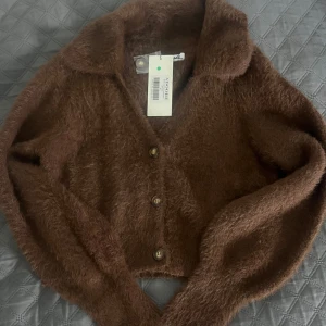 Brun stickad kofta från Adoore - Säljer en helt ny mysig brun stickad kofta från Adoore med knappar framtill. Ett måste i garderoben för höst och vinter!