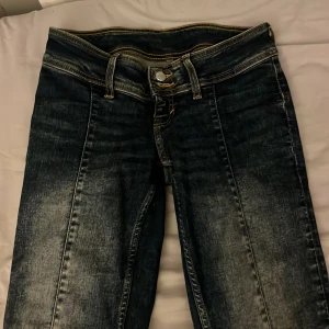 Mörkblå jeans med bootcut - Snygga mörkblå jeans med bootcut-stil och låg midja. De har två knappar där fram och en söm i mitten av benen. De är upp sprättade nertill pågrund av att byxorna va för korta för mig.