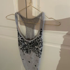 Grå linne med stjärnmönster - Snyggt grått linne med svart mönster av stjärnor och blommor. Perfekt för en avslappnad stil. Linnet har en racerback-design som ger en sportig känsla.
