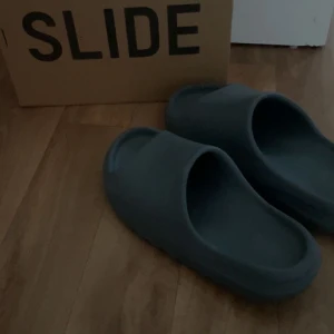 Grå YZY Slide från Adidas - Säljer ett par stilrena grå YZY Slide från Adidas. Perfekta för en avslappnad stil med en modern touch. De är bekväma och lätta att bära.  