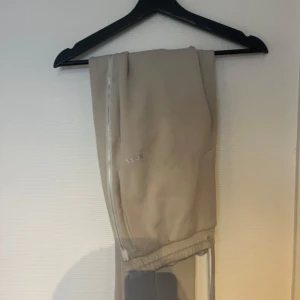 Beige byxor från BOSS - Snygga beige byxor från BOSS med diskret logga på sidan. Byxorna har en stilren design med elastisk midja. Perfekta för en avslappnad men stilfull look.