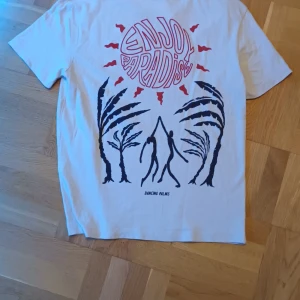 Vit t-shirt från Zara med tryck - Säljer en vit t-shirt från Zara med ett coolt tryck på baksidan som säger 'Enjoy Paradise' och 'Dancing Palms'. T-shirten har korta ärmar och är perfekt för en avslappnad stil.