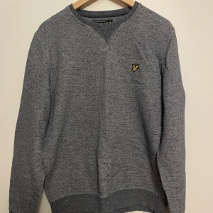 Grå tröja från Lyle & Scott - Säljer en stilren grå tröja från Lyle & Scott med deras ikoniska logga på bröstet. Tröjan har en klassisk passform. Perfekt för en avslappnad look. Tröjan är dessutom oanvänd